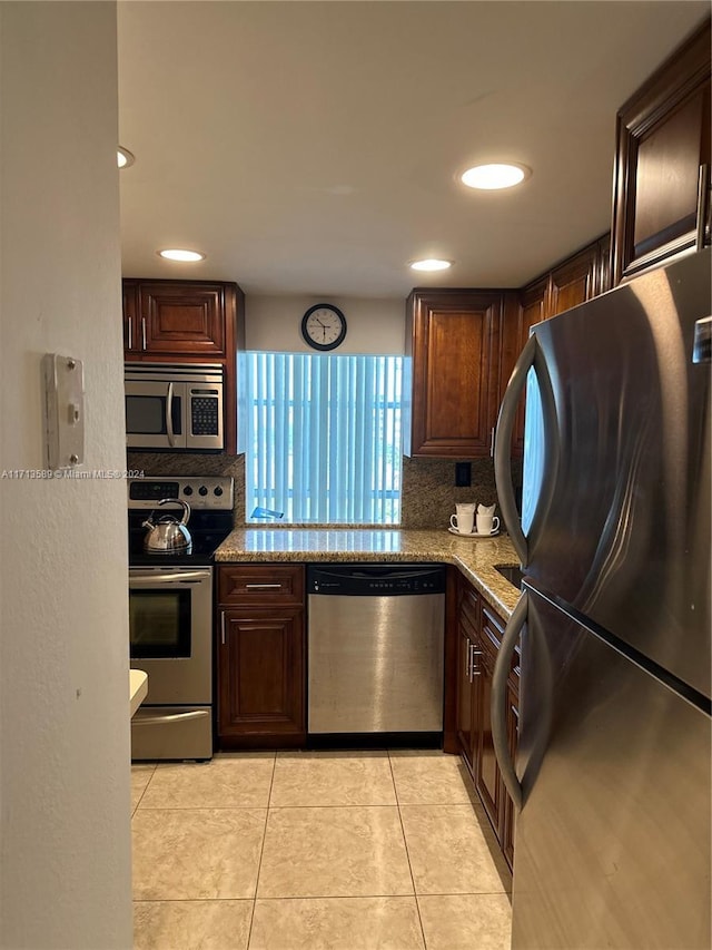 kitchen featuring decorative backsplash, light stone counters, light tile patterned floors, and stainless steel appliances