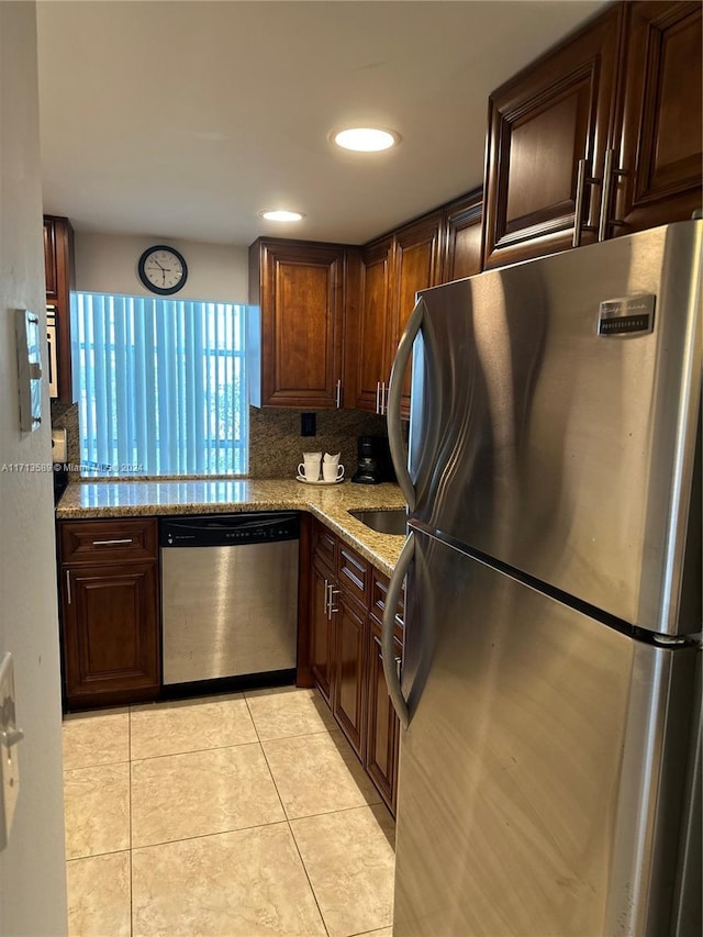 kitchen with backsplash, light stone countertops, stainless steel appliances, and light tile patterned floors