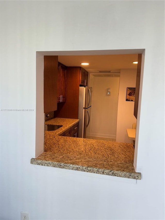 kitchen with kitchen peninsula, stainless steel refrigerator, light stone counters, and sink