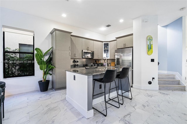 kitchen with a center island with sink, a kitchen breakfast bar, sink, dark stone countertops, and stainless steel appliances