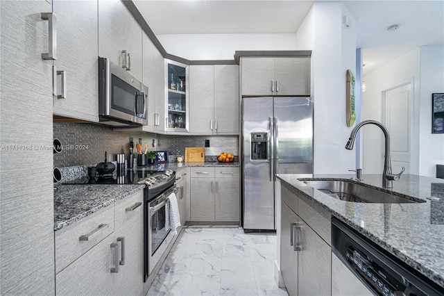 kitchen with appliances with stainless steel finishes, tasteful backsplash, dark stone counters, and sink