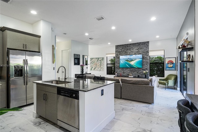 kitchen featuring sink, an island with sink, dark stone counters, and appliances with stainless steel finishes