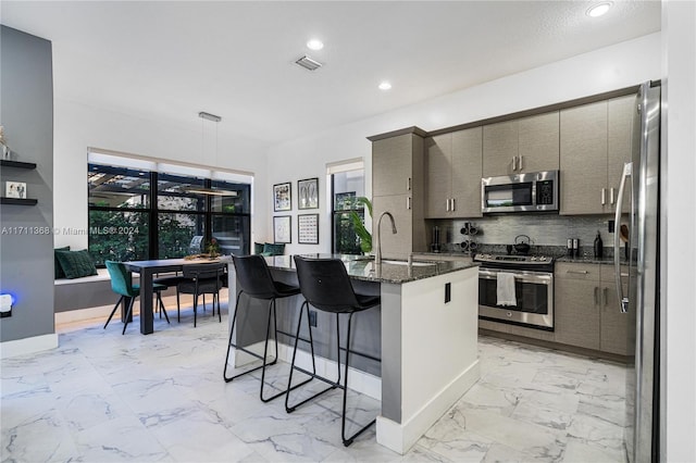 kitchen featuring a kitchen bar, appliances with stainless steel finishes, a kitchen island with sink, sink, and decorative light fixtures