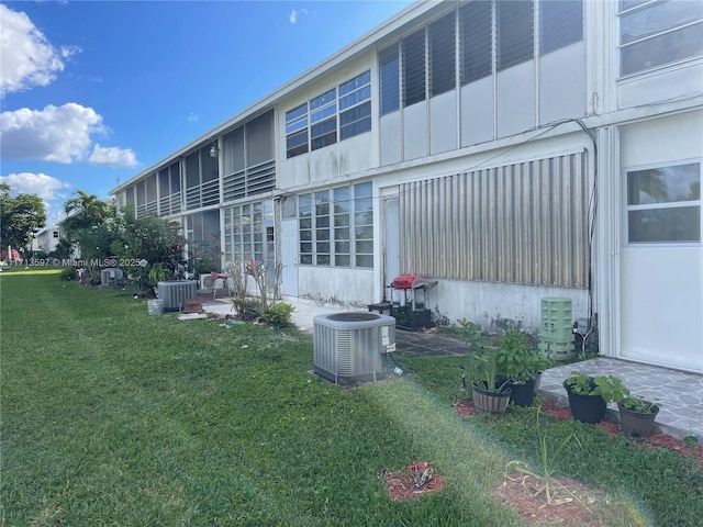 rear view of property with central AC unit and a lawn