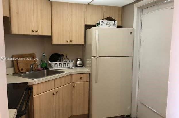 kitchen with light brown cabinetry, white fridge, and sink