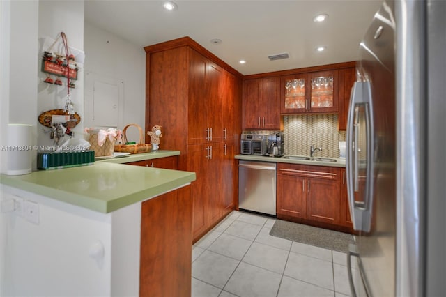 kitchen featuring sink, appliances with stainless steel finishes, tasteful backsplash, light tile patterned flooring, and kitchen peninsula