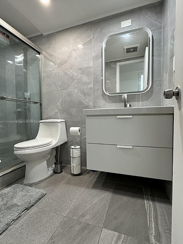 bathroom with a shower with door, vanity, tile walls, and toilet