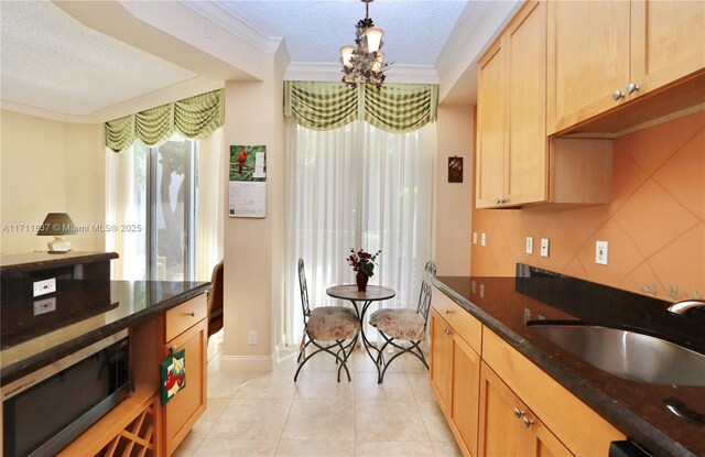 kitchen with ornamental molding, sink, dark stone countertops, and decorative light fixtures