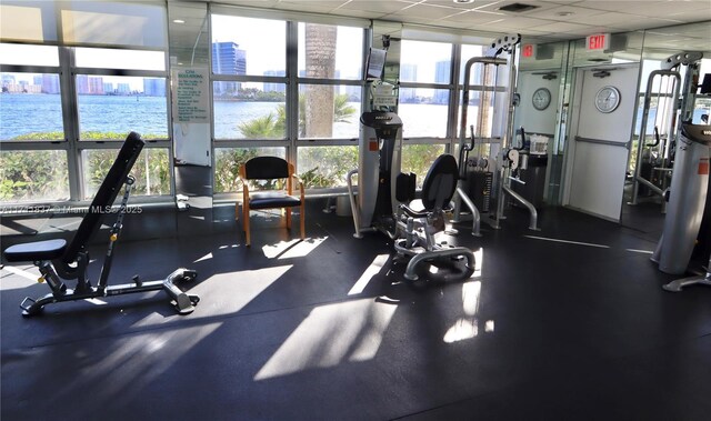 gym with expansive windows, a water view, a healthy amount of sunlight, and a drop ceiling