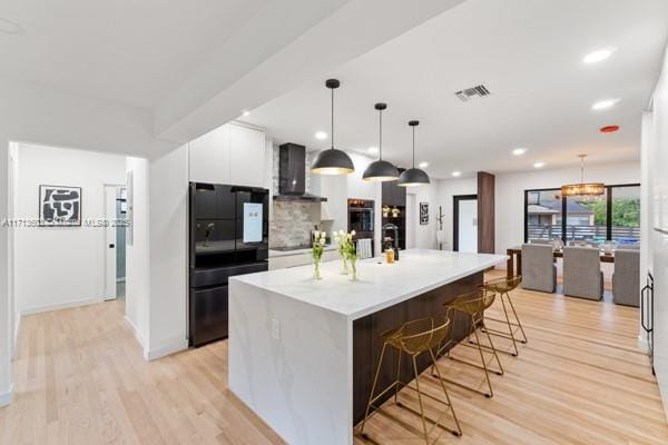 kitchen with wall chimney range hood, hanging light fixtures, a kitchen breakfast bar, a spacious island, and black appliances