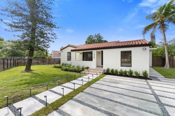 mediterranean / spanish house featuring a front lawn, fence, stucco siding, driveway, and a tile roof
