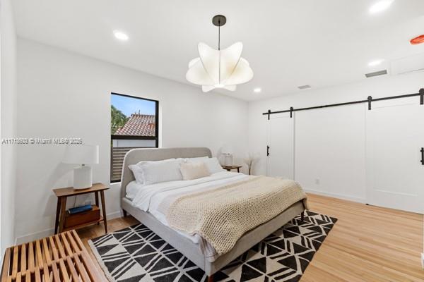 bedroom featuring recessed lighting, light wood finished floors, a barn door, and visible vents