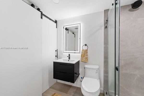 bathroom with hardwood / wood-style flooring, vanity, toilet, and a shower with shower door