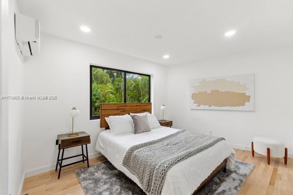bedroom with recessed lighting, a wall mounted air conditioner, light wood-style flooring, and baseboards
