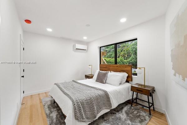 bedroom with recessed lighting, baseboards, a wall unit AC, and light wood finished floors