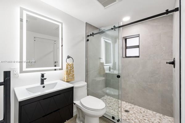 bathroom with vanity, a shower with door, and toilet