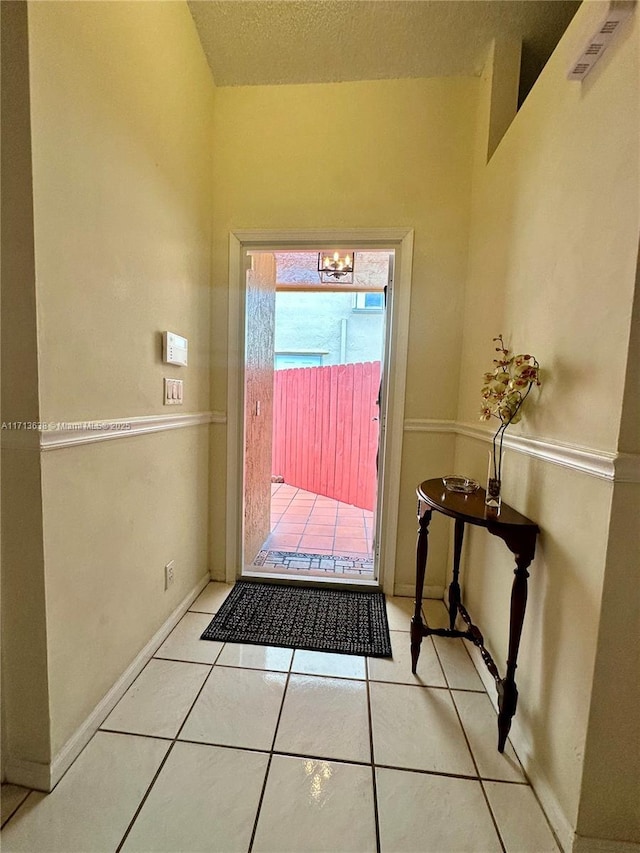 doorway featuring a chandelier, a textured ceiling, and light tile patterned flooring