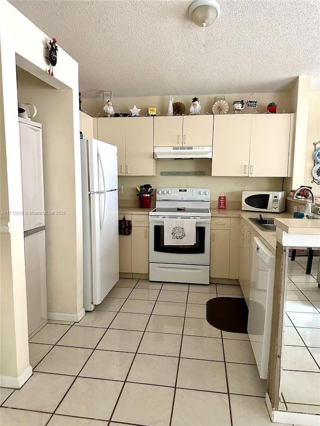 kitchen featuring cream cabinetry, light tile patterned flooring, white appliances, and a textured ceiling