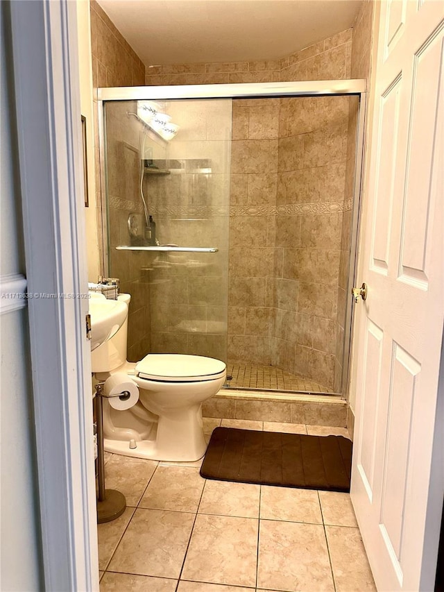 bathroom featuring tile patterned flooring, toilet, and a shower with shower door