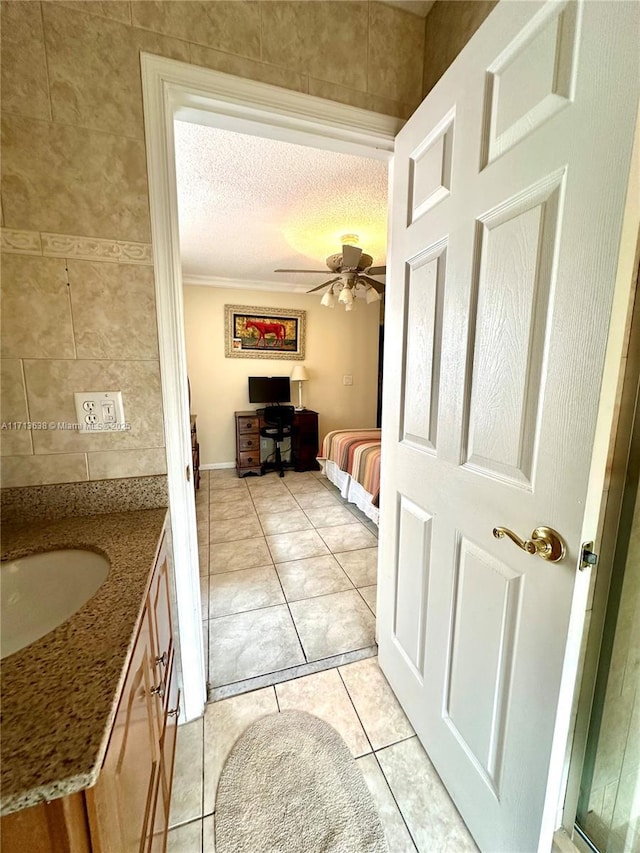 bathroom with ceiling fan, tile patterned flooring, a textured ceiling, vanity, and ornamental molding