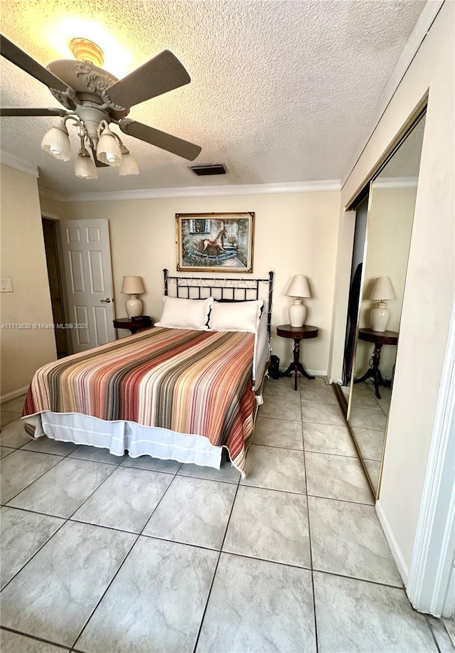 tiled bedroom with ceiling fan, ornamental molding, a textured ceiling, and a closet