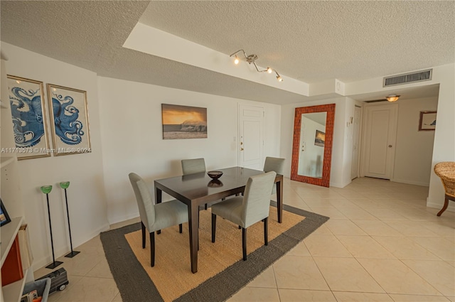 tiled dining area with a textured ceiling and a raised ceiling