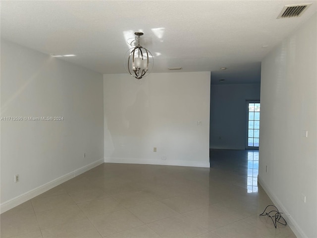 tiled spare room with a chandelier and a textured ceiling