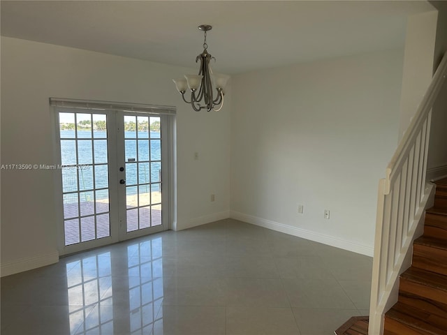 empty room featuring a water view, french doors, and an inviting chandelier