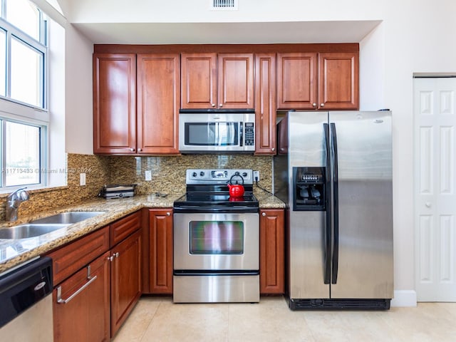 kitchen with light stone countertops, decorative backsplash, stainless steel appliances, sink, and light tile patterned floors