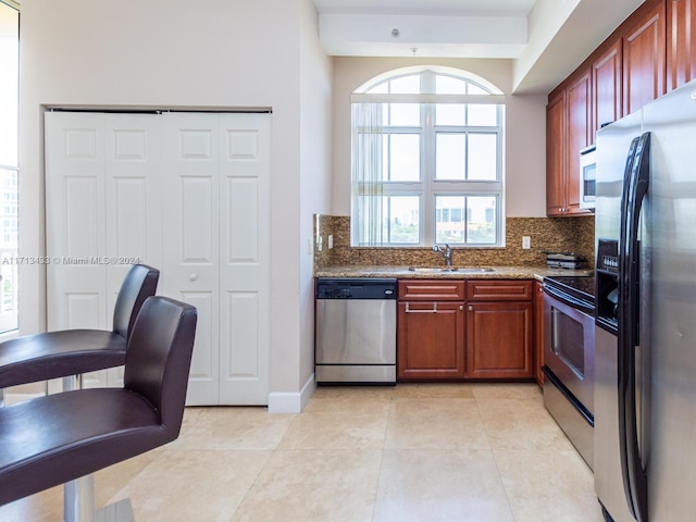 kitchen featuring backsplash, light stone counters, stainless steel appliances, sink, and light tile patterned floors