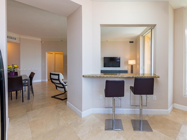 kitchen featuring light tile patterned flooring, ornamental molding, kitchen peninsula, and a breakfast bar area