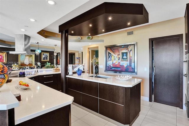 kitchen with light tile patterned flooring, dark brown cabinetry, sink, island range hood, and an island with sink