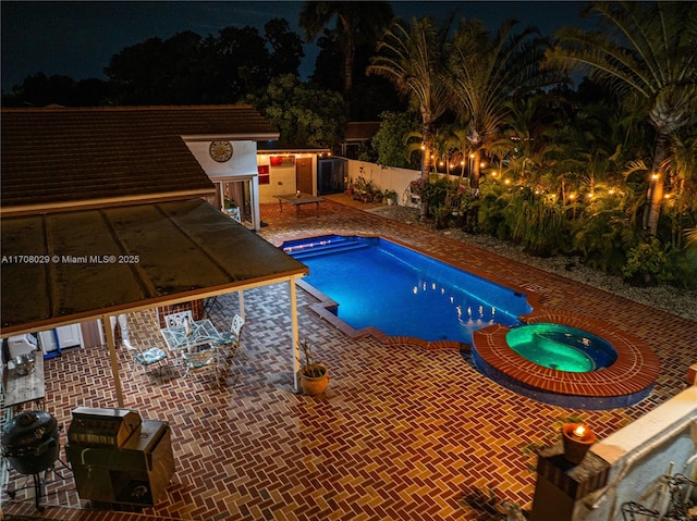 pool at night featuring a patio, area for grilling, and a pool with connected hot tub