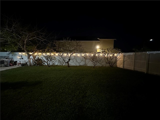 yard at night featuring a fenced backyard