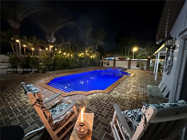 pool at night featuring a patio area and a fenced in pool