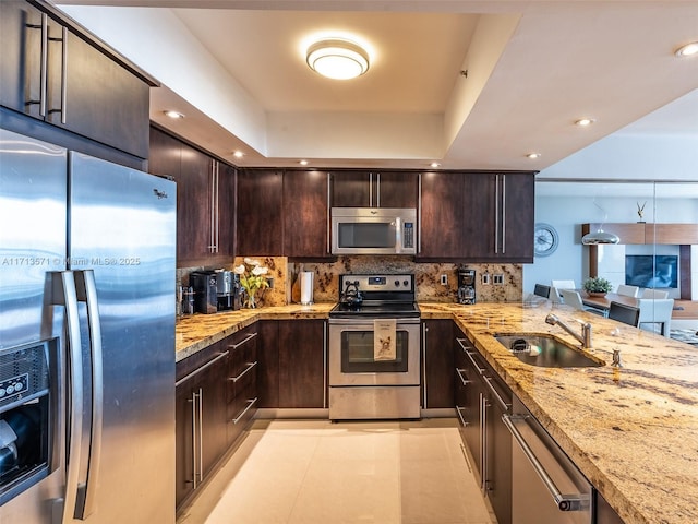 kitchen with tasteful backsplash, sink, light stone counters, kitchen peninsula, and stainless steel appliances