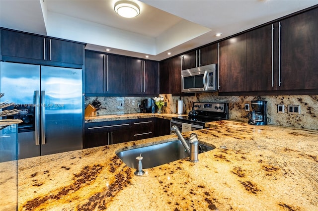 kitchen with sink, backsplash, light stone counters, stainless steel appliances, and dark brown cabinets