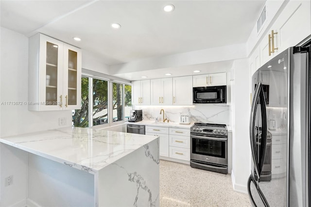 kitchen with kitchen peninsula, backsplash, light stone counters, stainless steel appliances, and white cabinetry