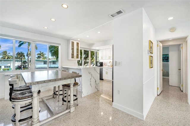 kitchen with light stone countertops, dishwasher, a kitchen island, a kitchen breakfast bar, and white cabinets