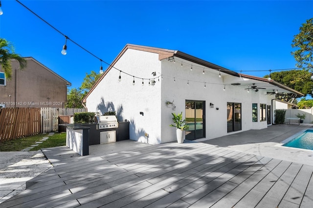 wooden deck with an outdoor kitchen, area for grilling, and a fenced in pool