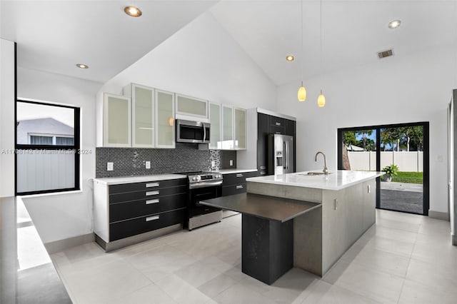 kitchen with high vaulted ceiling, a center island with sink, sink, appliances with stainless steel finishes, and decorative light fixtures