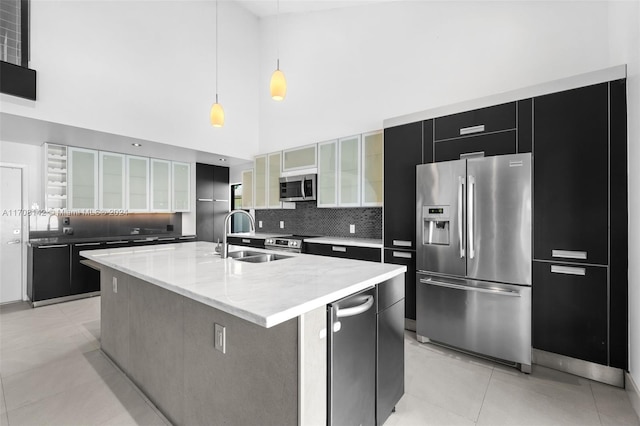 kitchen featuring a high ceiling, a center island with sink, sink, decorative light fixtures, and stainless steel appliances