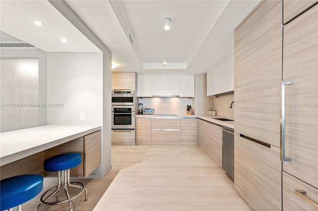 kitchen with white cabinetry, sink, stainless steel appliances, a raised ceiling, and a kitchen bar