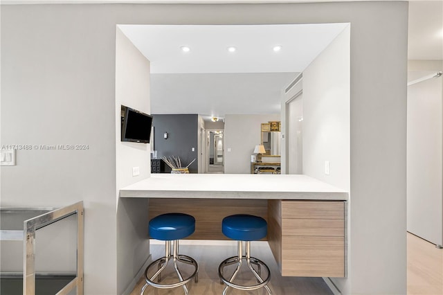 kitchen with a kitchen bar, kitchen peninsula, light brown cabinets, and light hardwood / wood-style flooring