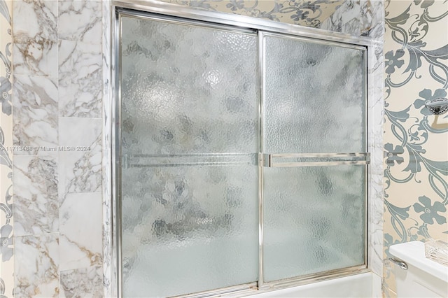 bathroom featuring toilet and bath / shower combo with glass door