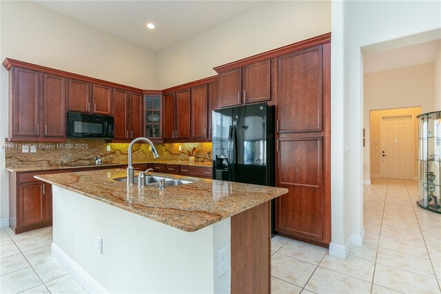 kitchen with a kitchen island with sink, sink, black appliances, and stone countertops