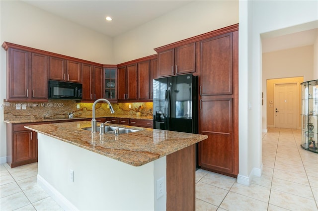 kitchen featuring an island with sink, sink, stone countertops, and black appliances