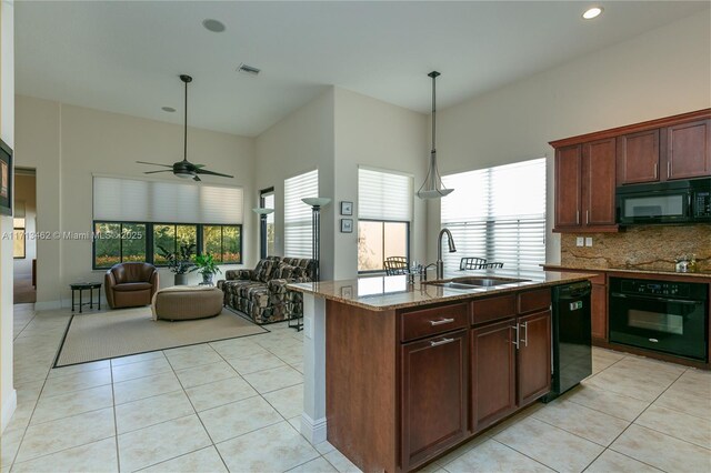 kitchen with light tile patterned flooring, an island with sink, sink, light stone counters, and black appliances