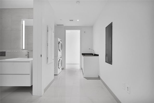 corridor with electric panel, stacked washer and dryer, and sink