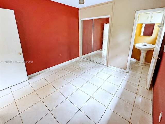 unfurnished bedroom with connected bathroom, a closet, and light tile patterned flooring